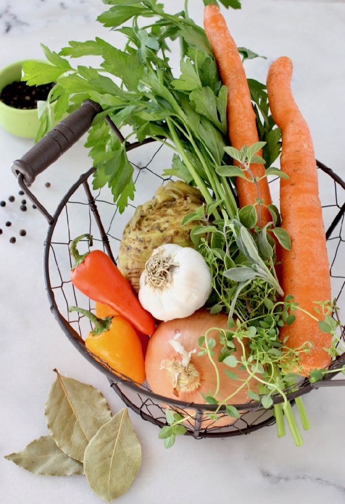 Basket of aromatics: carrot, onion, celery, parsley, celery root, peppers, garlic and herbs.